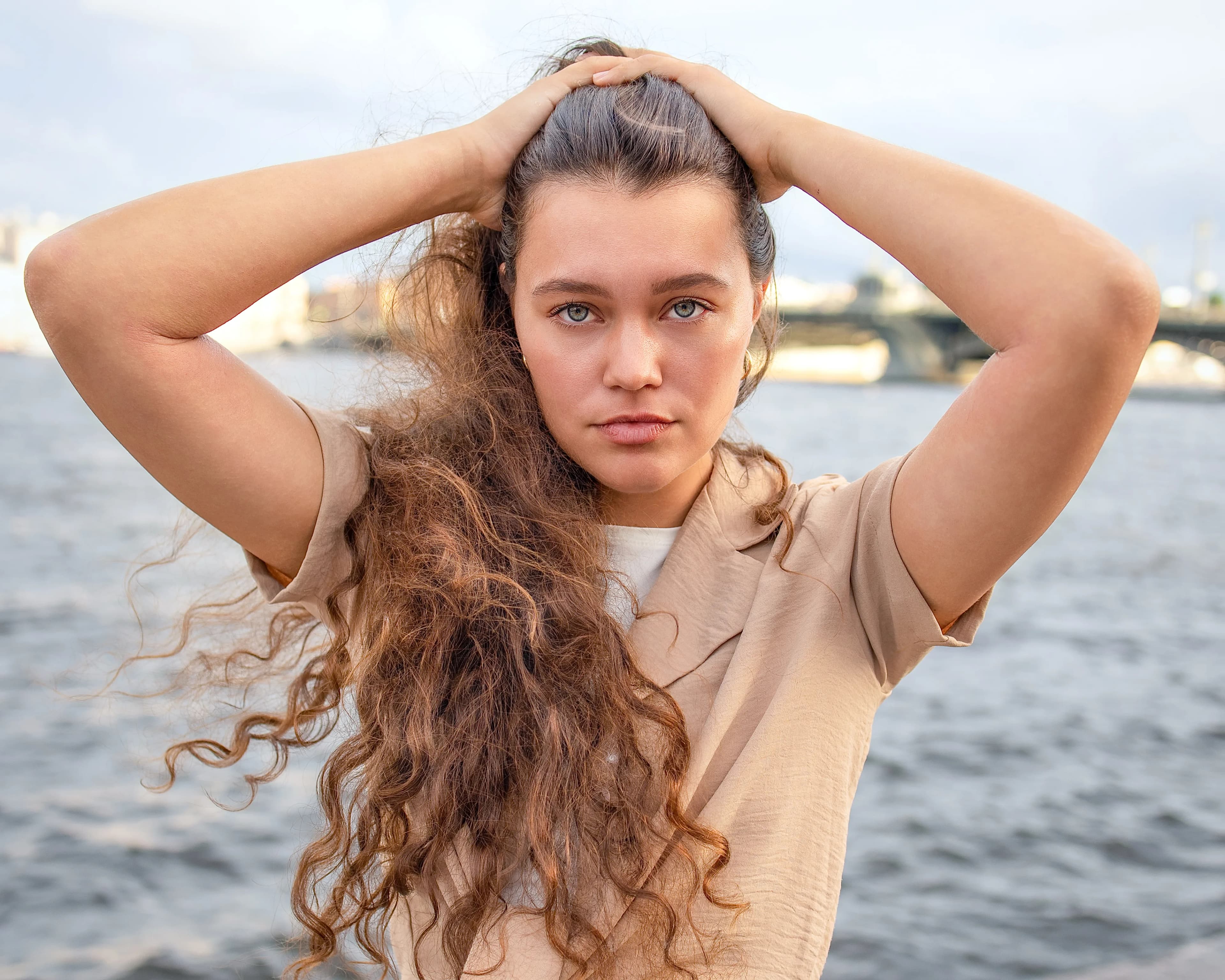 Lady by river with curly hair hands on head