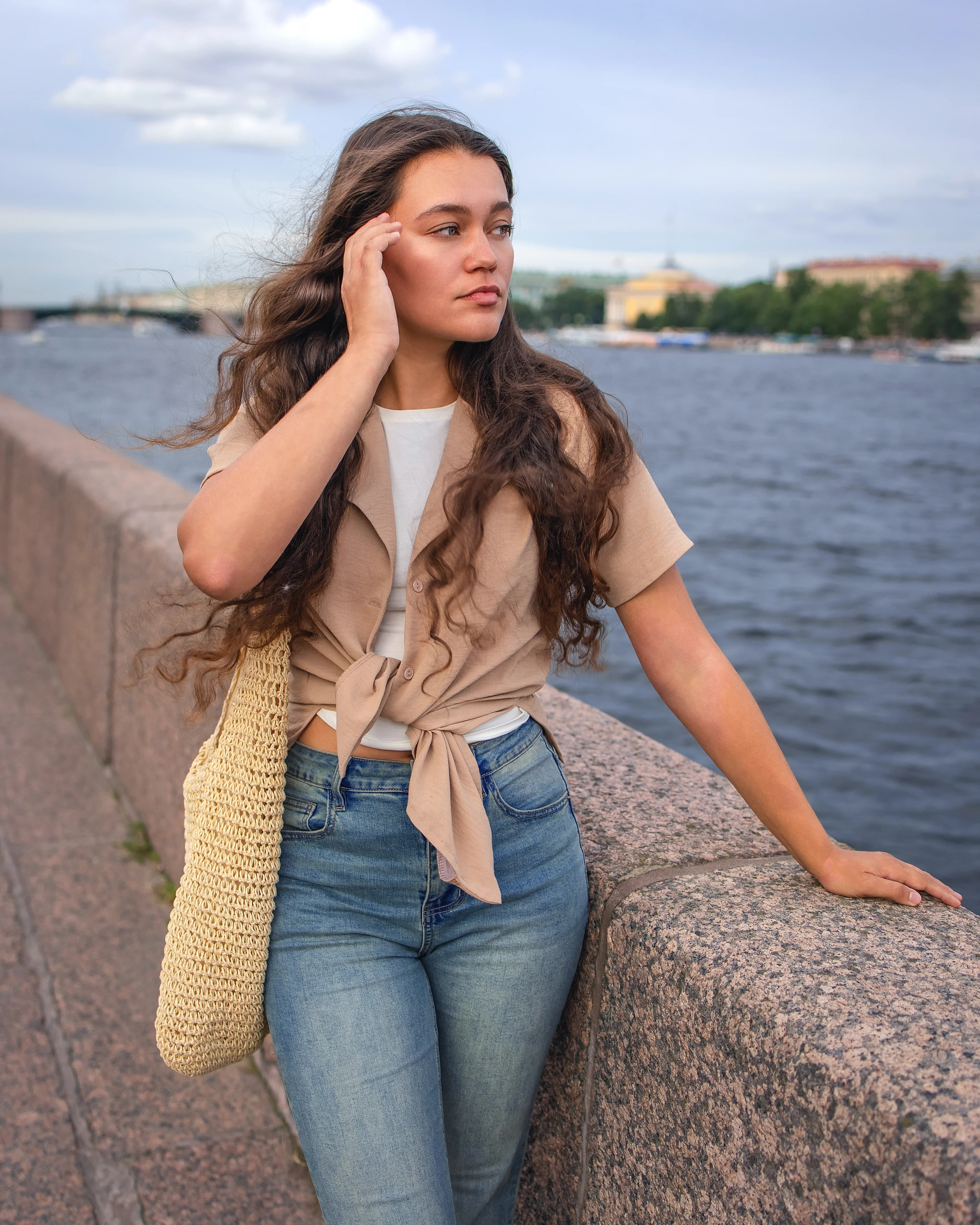 Lady standing by river touching her curly hair